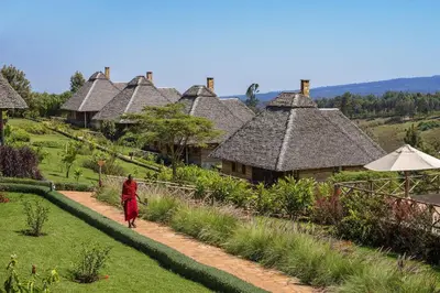 a woman walking down a path in front of a village at Neptune Ngorongoro Luxury Lodge - All Inclusive in Ngorongoro