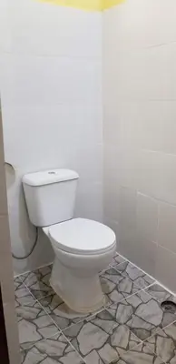 a white toilet in a bathroom with a tile floor at Aivlys Lodge Kilimanjaro in Msaranga