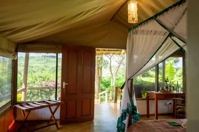a bedroom in a tent with a view of the forest at Karatu Tented Lodge in Karatu
