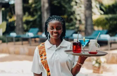 a woman holding a tray with two drinks on it at Chanya by Ardhi Africa in Moshi
