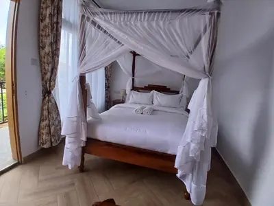 a bedroom with a canopy bed with white sheets and pillows at Bird of Paradise Eco Lodge in Arusha