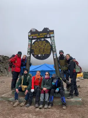 a group of people posing in front of a sign at Mai Kilimanjaro Home Stay in Marangu