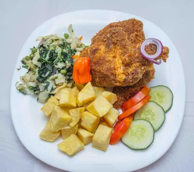 a plate of food with chicken and vegetables and a salad at Panone Hotels - King'ori Kilimanjaro Airport in Moshi