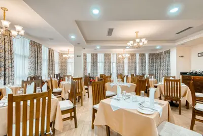 a restaurant with white tables and chairs and curtains at Kibo Palace Hotel Moshi in Moshi
