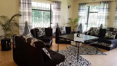 a living room with couches and a table and windows at The House of Black and White in Arusha
