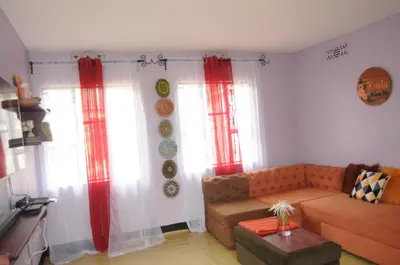 a living room with a couch and two windows at Hakuna Matata Cozy Apartment in Karatu
