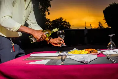 a person pouring a glass of wine on a table at Randa Cottages Moshi in Kirua