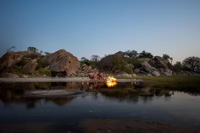 a group of people standing around a fire next to a body of water at Kisima Ngeda Camp in Mangola