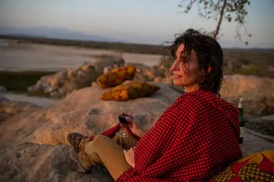 a woman sitting on a rock holding a glass of wine at Kisima Ngeda Camp in Mangola
