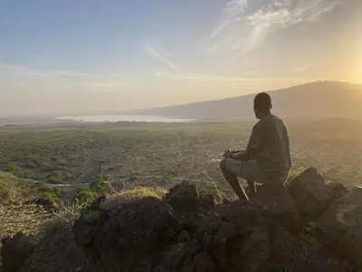 a man sitting on a rock looking out over a valley at Lake Natron Maasai Guesthouse in Mtowabaga
