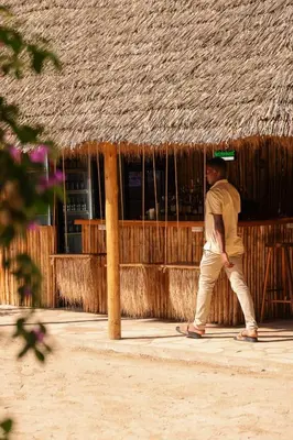 a man walking in front of a thatched building at The Jungle Pearl Resort in Mto wa Mbu