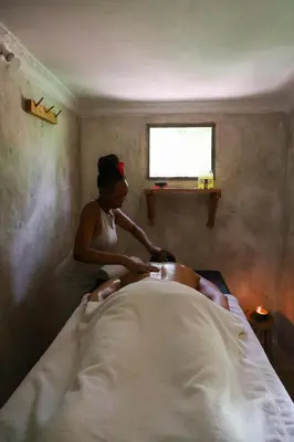a woman cutting a mans hair on a bed at The Jungle Pearl Resort in Mto wa Mbu