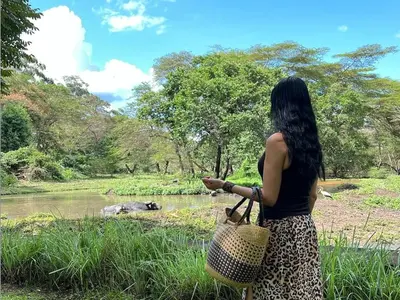 a woman standing in front of a river looking at aigator at Mount Meru Game Lodge in Arusha